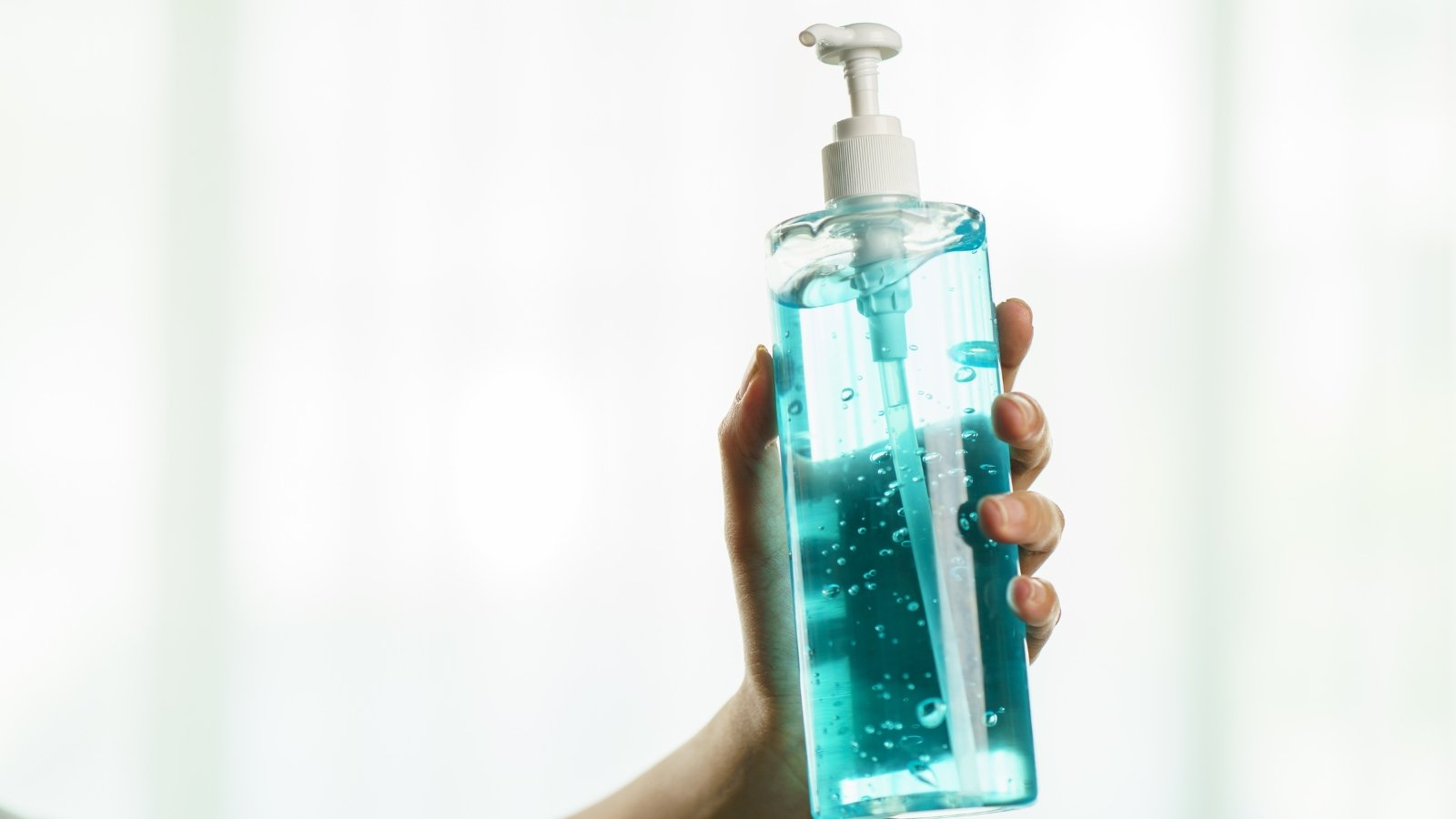 A clear bottle of isopropyl alcohol with a pump-top dispenser held by a hand, ready for use in sterilization tasks.