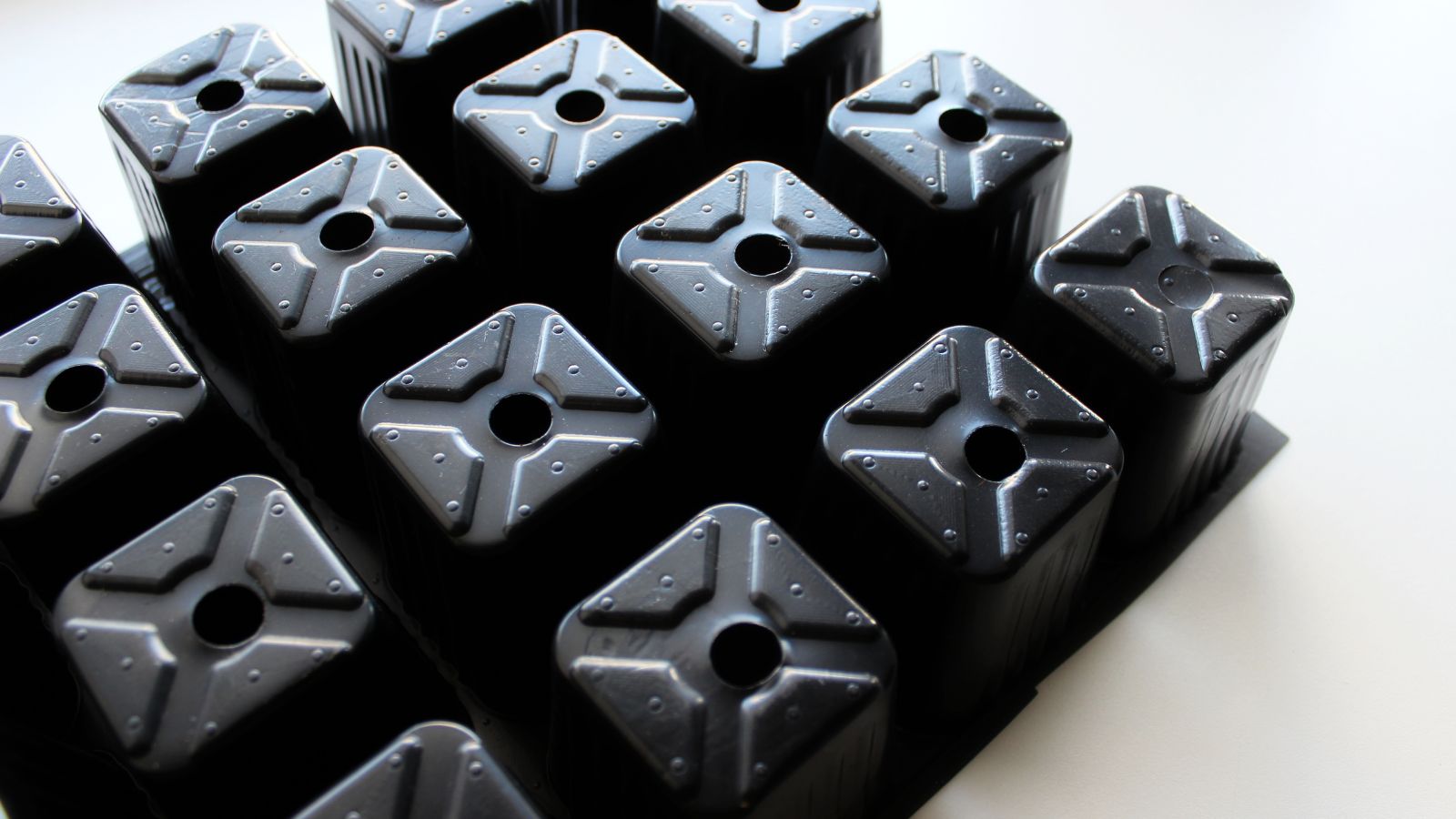A black seed tray with holes turned upside down placed on a pure white surface