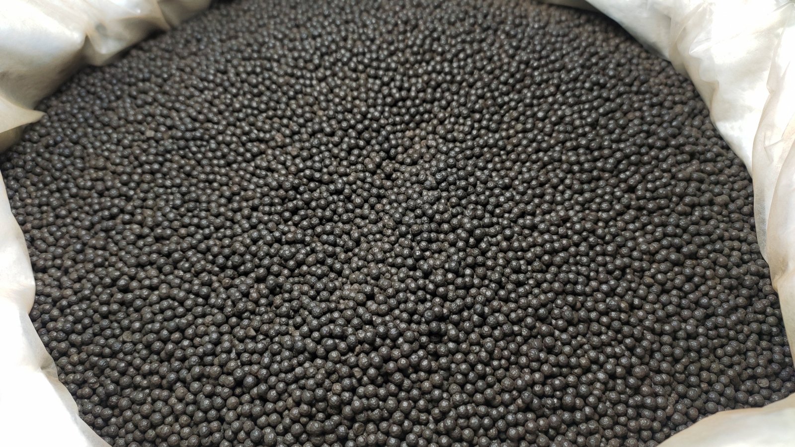 In a white sack, black slow-release granules of organic fertilizer nestle, promising steady nourishment for plants. Each granule is carefully formulated to release nutrients gradually, ensuring sustained growth and health for the plants.