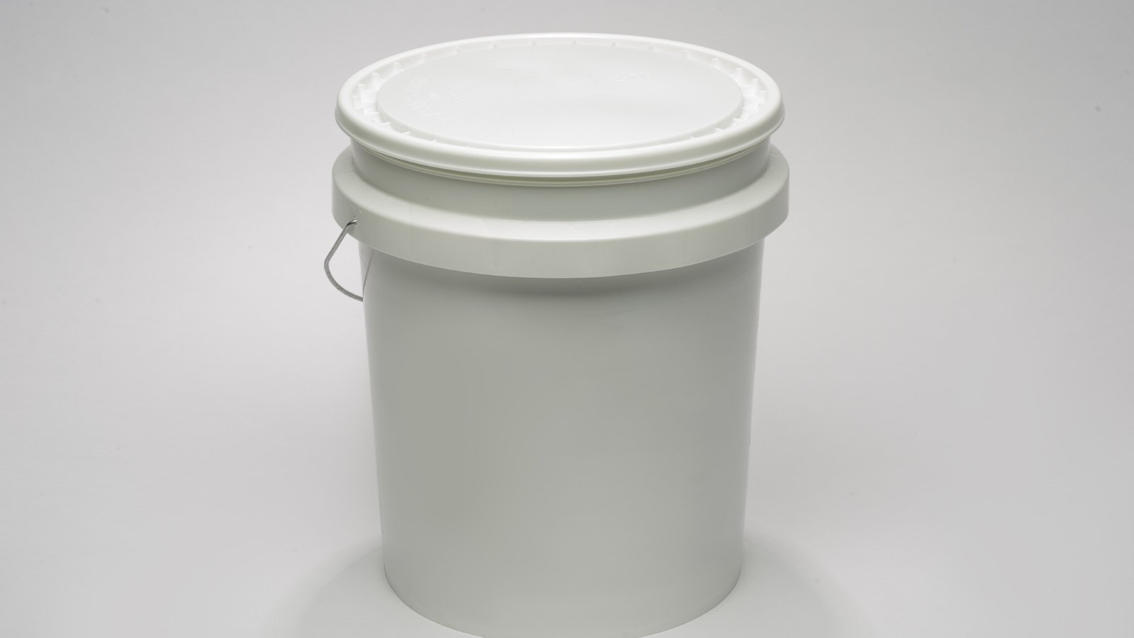A simple white plastic bucket with a metal handle placed against a neutral background, useful for storing growing materials.