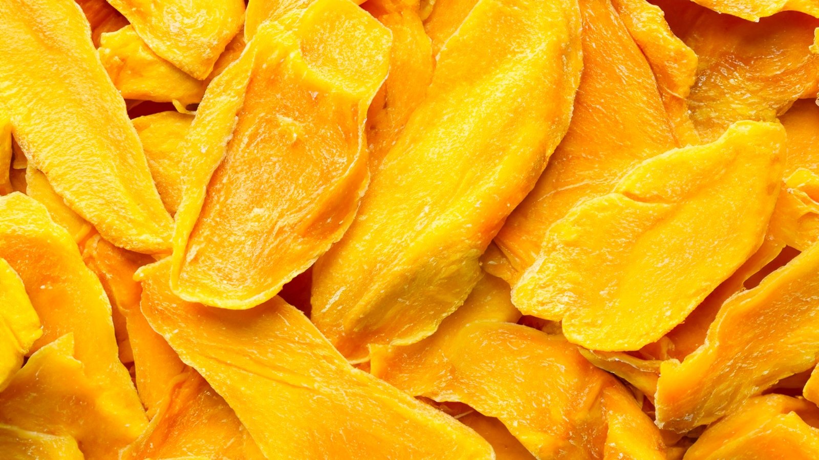 Close-up of dried mango fruit slices that showcase a vibrant orange-yellow color with a slightly wrinkled texture.