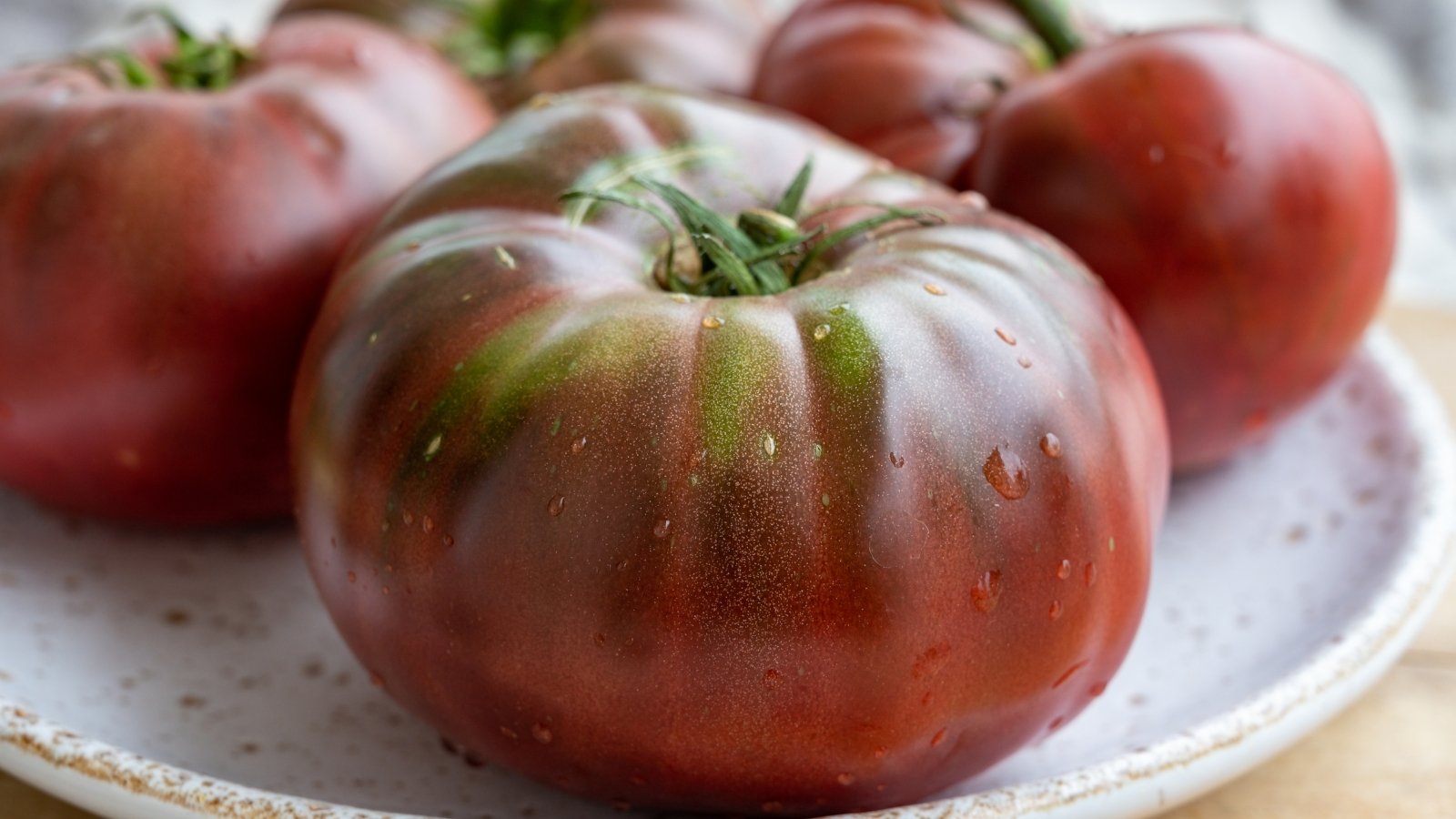 A close-up of ripe 'Black Krim' tomatoes arranged beautifully on a clean white ceramic plate.