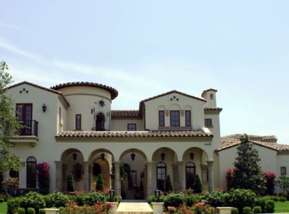 A spanish style home with beautiful gardens on a sunny day.