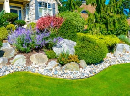 A beige, blue, and rock-walled home features beautiful rock bed gardens.