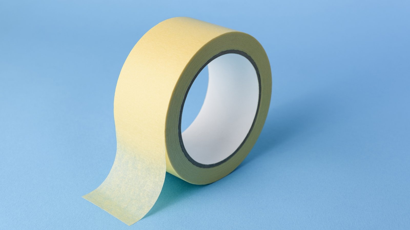 A single roll of light-yellow adhesive tape placed on a smooth blue surface, ideal for sealing tasks.